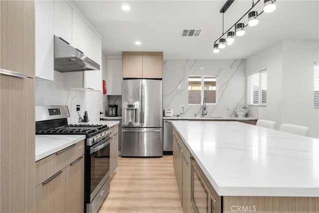 kitchen featuring sink, hanging light fixtures, stainless steel appliances, white cabinets, and a kitchen island