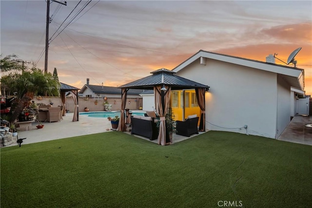 back house at dusk with a gazebo, a patio area, and a lawn