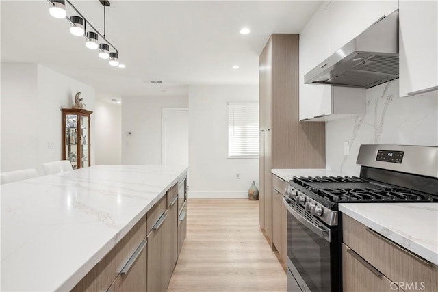 kitchen featuring stainless steel range with gas cooktop, white cabinetry, decorative backsplash, hanging light fixtures, and wall chimney range hood