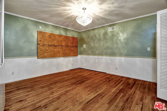 spare room featuring wood-type flooring, a notable chandelier, and crown molding