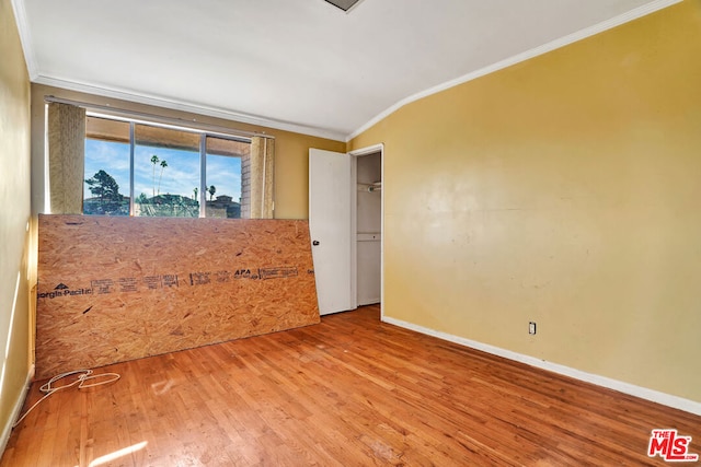 empty room with lofted ceiling, hardwood / wood-style floors, and ornamental molding