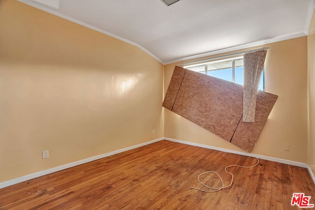 empty room featuring wood-type flooring, lofted ceiling, and ornamental molding