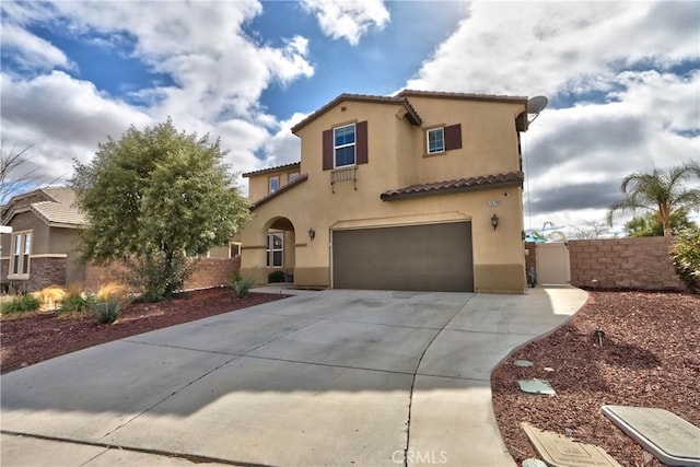 mediterranean / spanish-style home featuring stucco siding, concrete driveway, fence, a garage, and a tiled roof