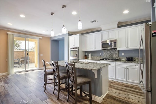 kitchen featuring appliances with stainless steel finishes, decorative light fixtures, an island with sink, and white cabinets