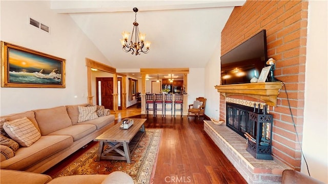 living room with dark hardwood / wood-style floors, high vaulted ceiling, beamed ceiling, a brick fireplace, and an inviting chandelier