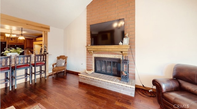 living room featuring dark wood-type flooring, lofted ceiling, a fireplace, and an inviting chandelier