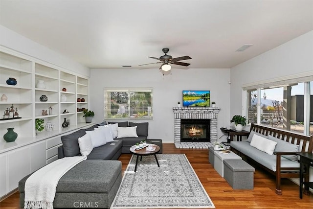 living room with wood-type flooring, a brick fireplace, a wealth of natural light, and ceiling fan