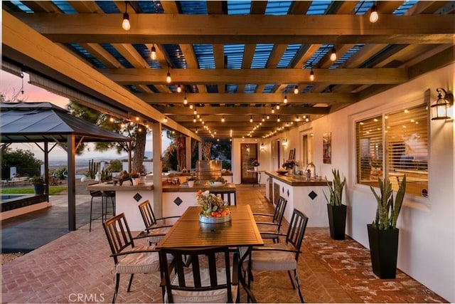 patio terrace at dusk featuring a bar, a gazebo, and a pergola