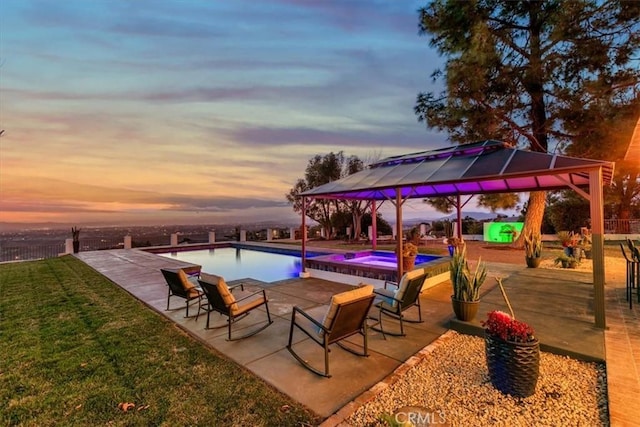 pool at dusk with a gazebo, an in ground hot tub, a patio, and a lawn