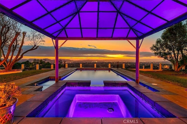 pool at dusk featuring a mountain view and an in ground hot tub