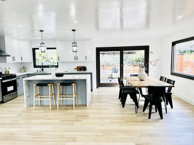 kitchen with stainless steel gas range oven, white cabinetry, hanging light fixtures, light wood-type flooring, and a kitchen island