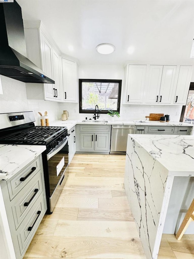 kitchen with sink, white cabinets, stainless steel appliances, light stone countertops, and wall chimney exhaust hood