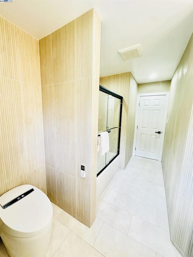 bathroom featuring toilet, a shower with shower door, tile patterned flooring, and tile walls