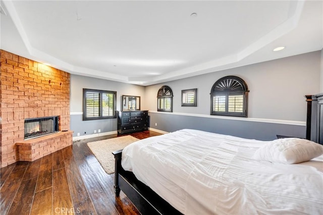 bedroom with a tray ceiling, dark hardwood / wood-style flooring, and a brick fireplace