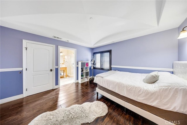 bedroom with vaulted ceiling, dark wood-type flooring, and connected bathroom