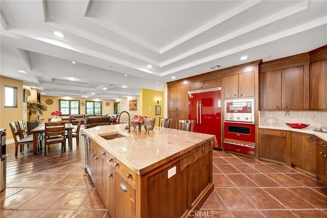 kitchen featuring sink, a kitchen island with sink, tasteful backsplash, a tray ceiling, and paneled built in fridge