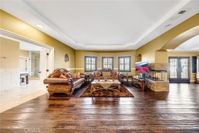 living room with a raised ceiling, a multi sided fireplace, dark wood-type flooring, and french doors