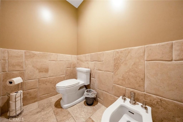 bathroom with a bidet, sink, toilet, and tile walls