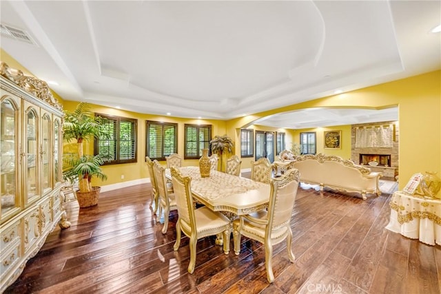 dining area with a fireplace, a tray ceiling, and dark wood-type flooring