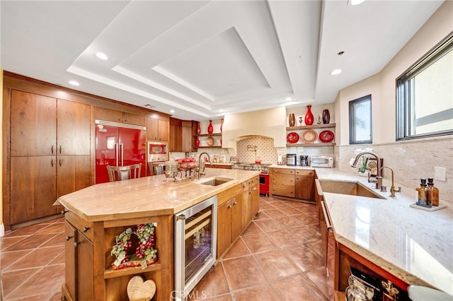 kitchen featuring sink, a kitchen island with sink, a tray ceiling, custom exhaust hood, and beverage cooler