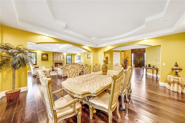 dining space featuring hardwood / wood-style floors, a large fireplace, and a raised ceiling