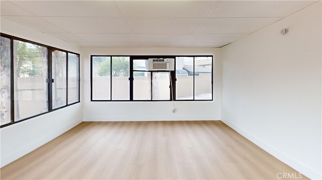 interior space featuring a paneled ceiling, an AC wall unit, and light wood-type flooring