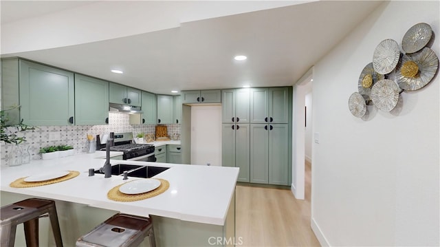 kitchen featuring green cabinets, stainless steel gas range, a kitchen breakfast bar, and kitchen peninsula