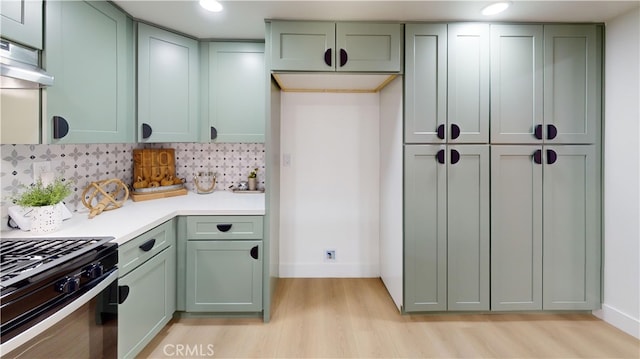 kitchen with black range with gas cooktop, backsplash, light hardwood / wood-style floors, and green cabinetry