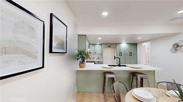 kitchen featuring sink, kitchen peninsula, a kitchen breakfast bar, and green cabinetry