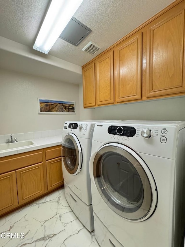 laundry room with cabinets, separate washer and dryer, sink, and a textured ceiling