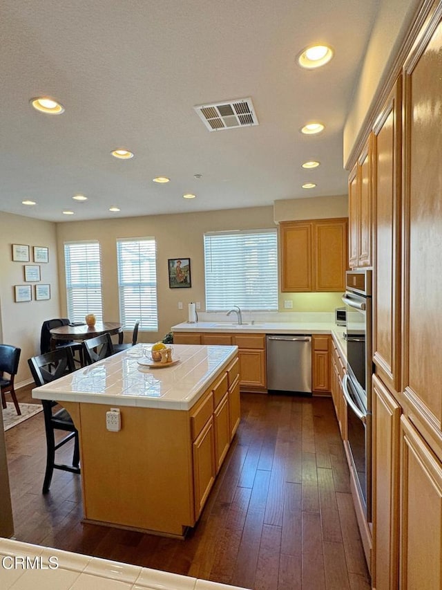 kitchen with dark hardwood / wood-style flooring, tile counters, a center island, and appliances with stainless steel finishes