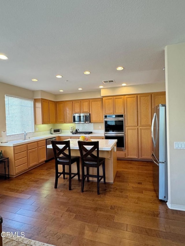 kitchen with a kitchen island, a breakfast bar, dark hardwood / wood-style floors, stainless steel appliances, and a textured ceiling