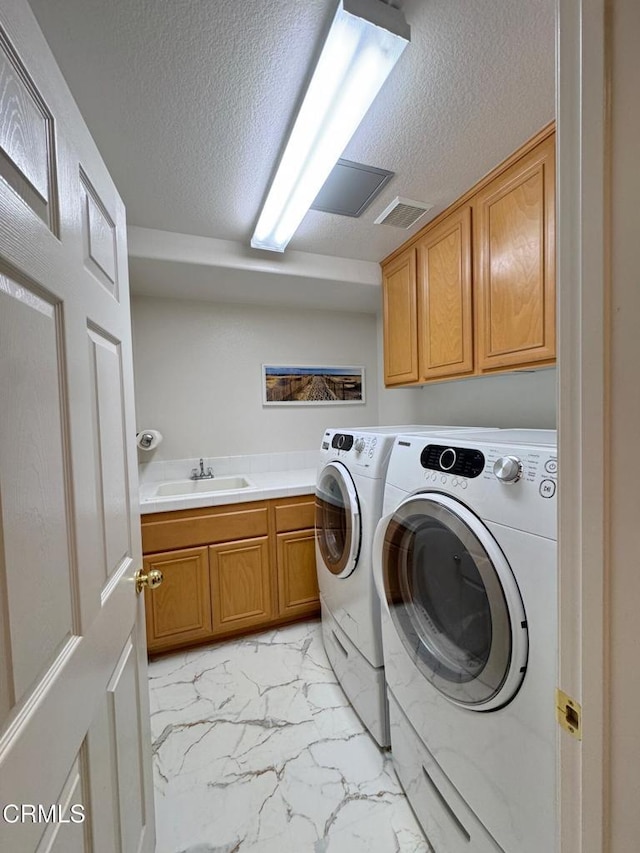 laundry area with sink, a textured ceiling, cabinets, and washing machine and clothes dryer