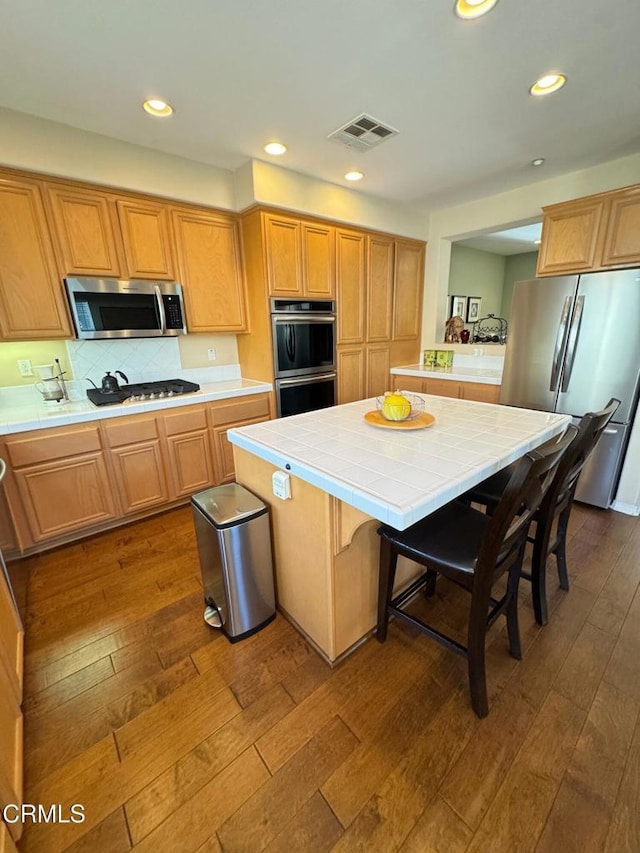 kitchen featuring a kitchen island, tile countertops, a kitchen breakfast bar, stainless steel appliances, and dark wood-type flooring