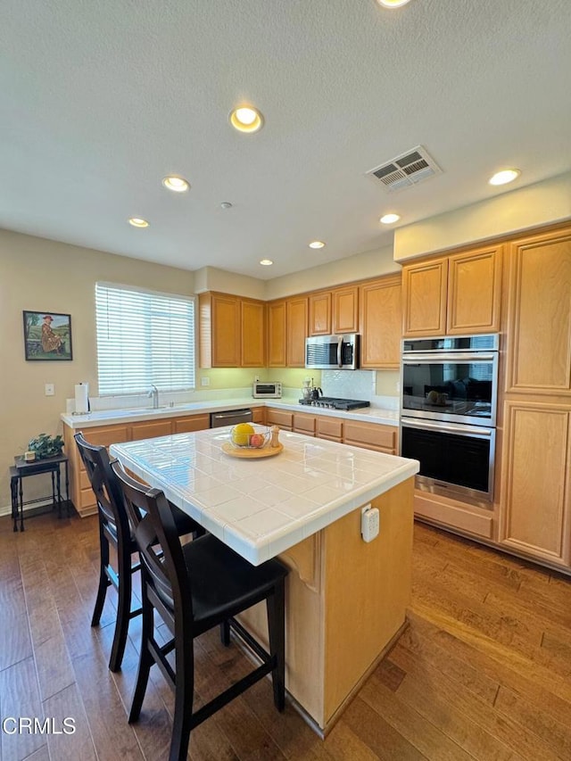 kitchen featuring appliances with stainless steel finishes, tile counters, a center island, and hardwood / wood-style floors