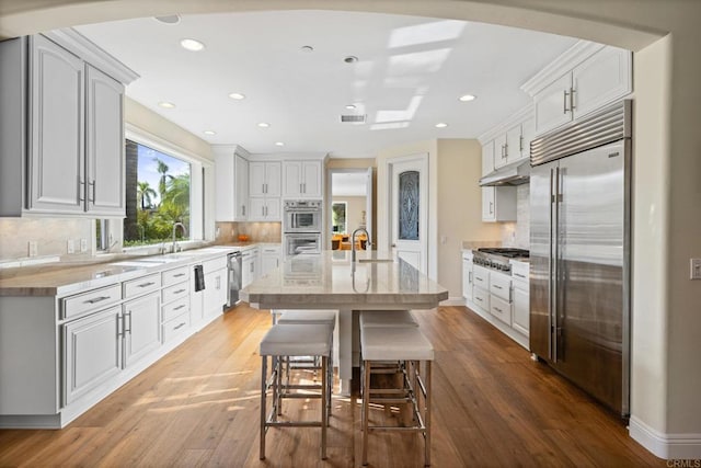 kitchen featuring a breakfast bar, white cabinetry, a center island, appliances with stainless steel finishes, and hardwood / wood-style floors