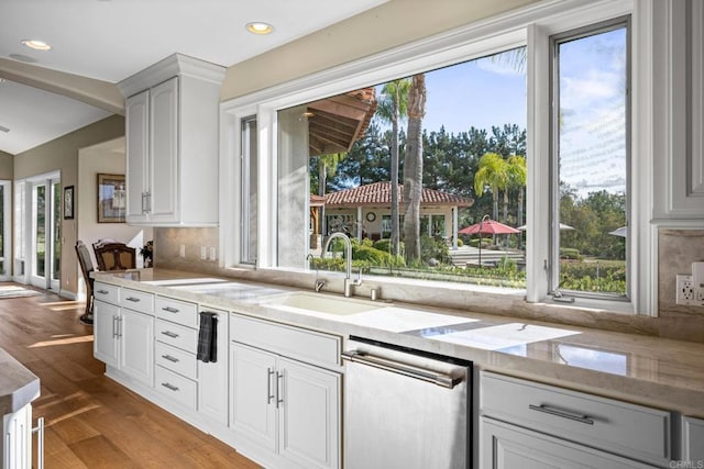 kitchen with sink, light stone counters, light wood-type flooring, stainless steel dishwasher, and white cabinets