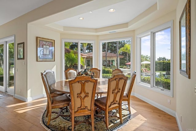 dining area with a tray ceiling, plenty of natural light, and light wood-type flooring