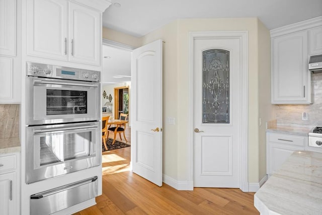 kitchen featuring white cabinetry, light wood-type flooring, stainless steel double oven, light stone countertops, and backsplash