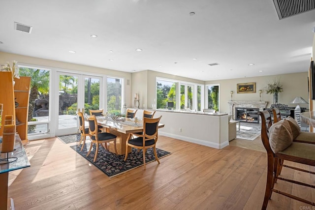 dining room with a high end fireplace, plenty of natural light, light hardwood / wood-style floors, and french doors