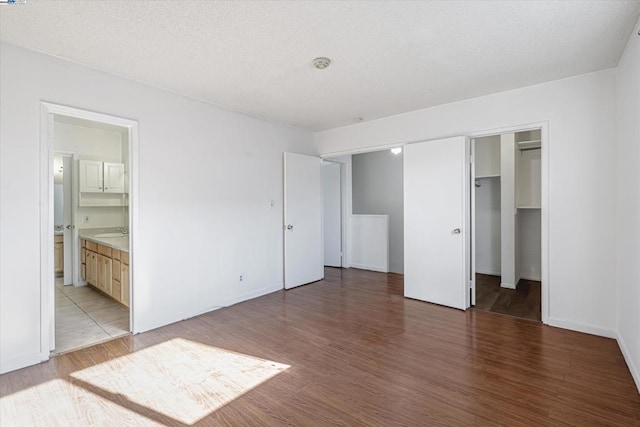 unfurnished bedroom with sink, a spacious closet, wood-type flooring, and ensuite bathroom