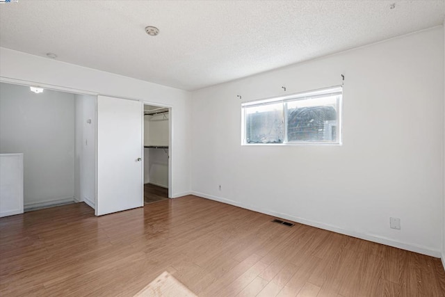 unfurnished bedroom with wood-type flooring, a walk in closet, a textured ceiling, and a closet