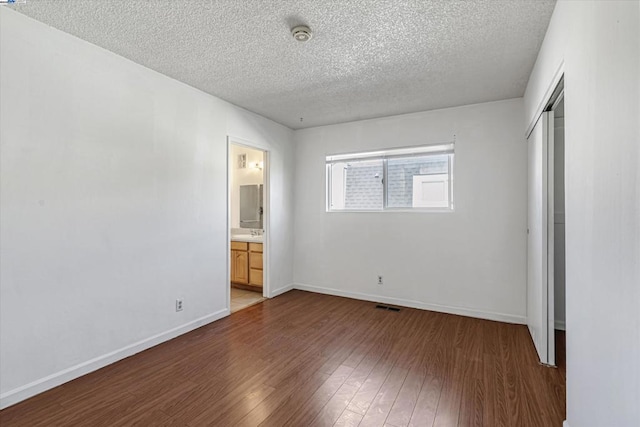 unfurnished bedroom featuring hardwood / wood-style flooring, ensuite bath, a closet, and a textured ceiling