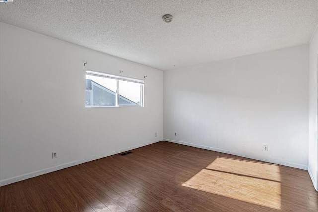 empty room with dark wood-type flooring and a textured ceiling