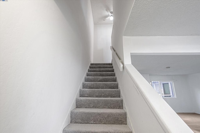 stairway with wood-type flooring and a textured ceiling