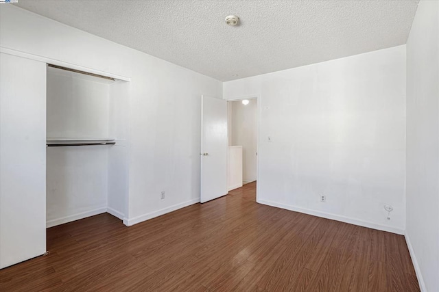 unfurnished bedroom with a textured ceiling, dark hardwood / wood-style flooring, and a closet