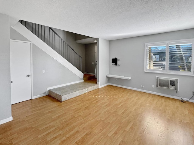 unfurnished living room with a wall unit AC, a textured ceiling, and light hardwood / wood-style floors