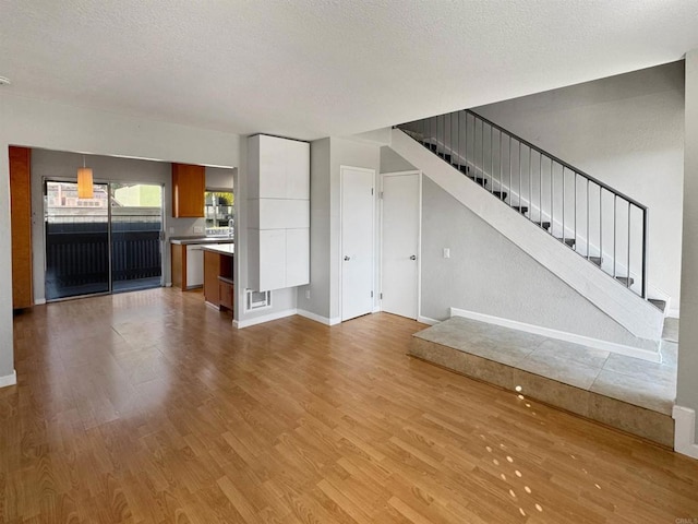 unfurnished living room with light hardwood / wood-style flooring and a textured ceiling