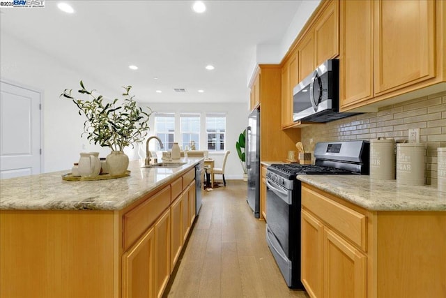 kitchen with sink, backsplash, stainless steel appliances, light hardwood / wood-style floors, and a center island with sink