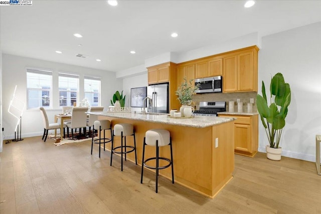 kitchen featuring a breakfast bar, a center island with sink, appliances with stainless steel finishes, light hardwood / wood-style floors, and backsplash